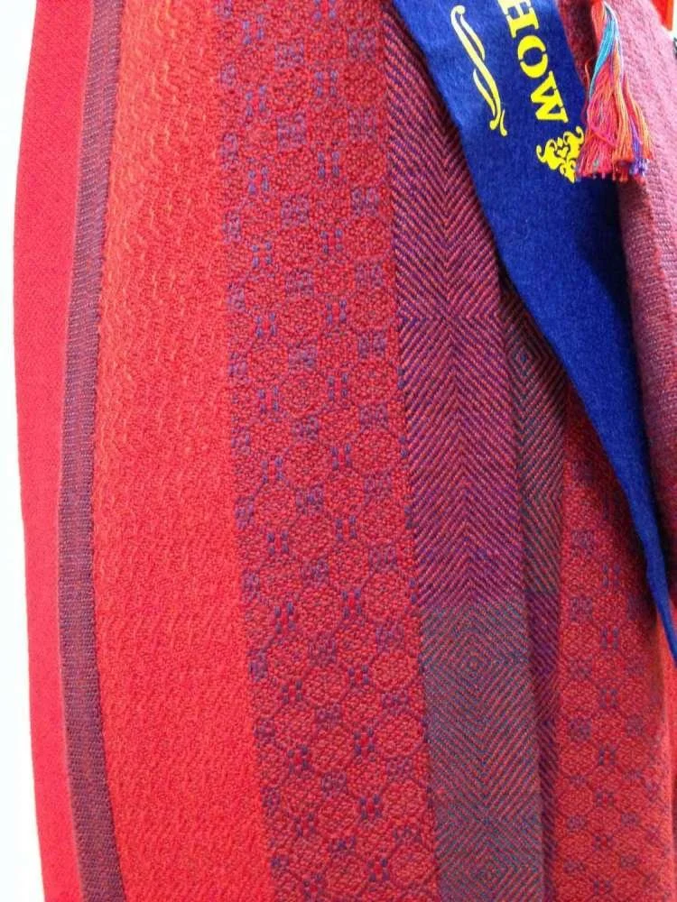 Close-up of colorful woven textile or towel with various intricate patterns and a small part of a blue fabric with yellow text and colorful fringes.
