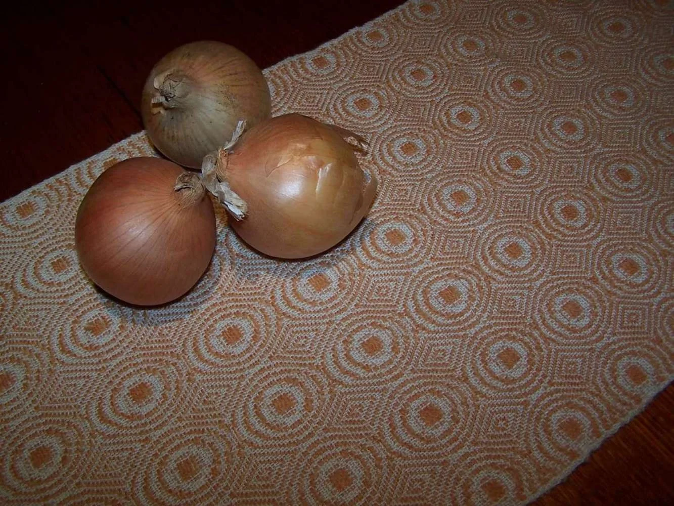 Three onions placed on a patterned cloth surface with a wooden background.