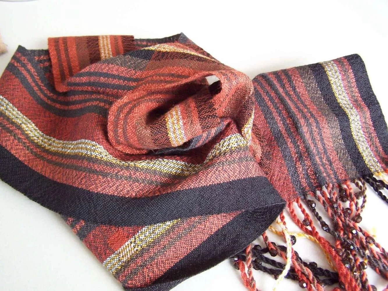 A red and black plaid woven scarf with yellow and white accents, displayed on a white surface.
