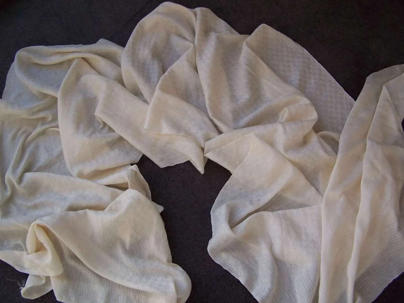 Cream-colored, sheer fabric draped and gathered on a dark surface.