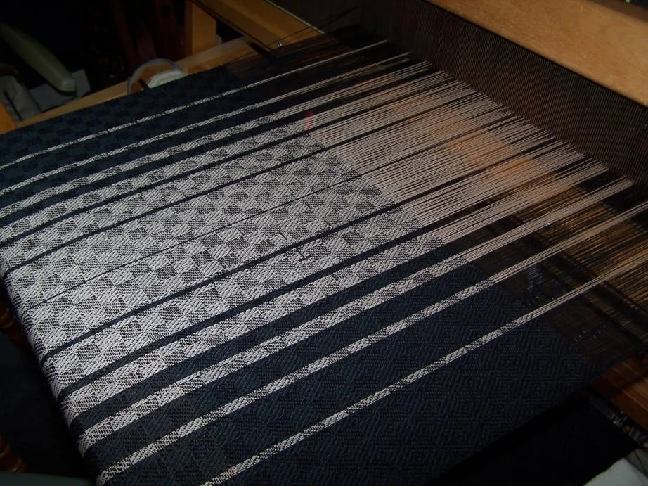 A weaving loom with a partially woven black and white patterned textile.