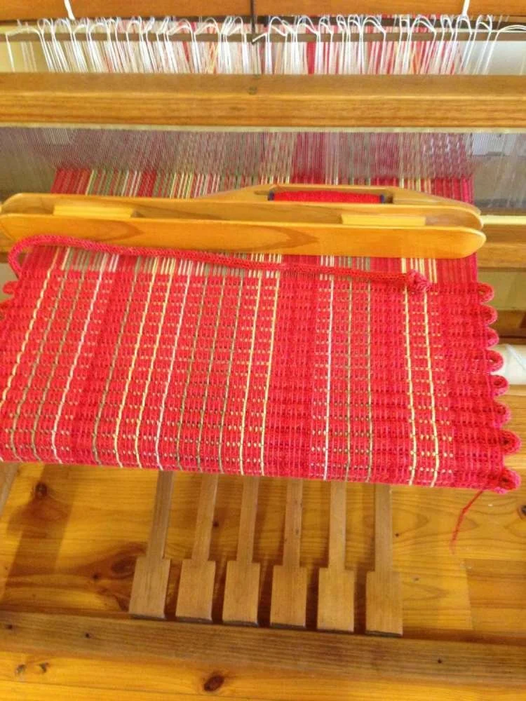 A wooden sled with a red woven blanket draped over it inside a room with a wooden floor and a wooden structure in the background.