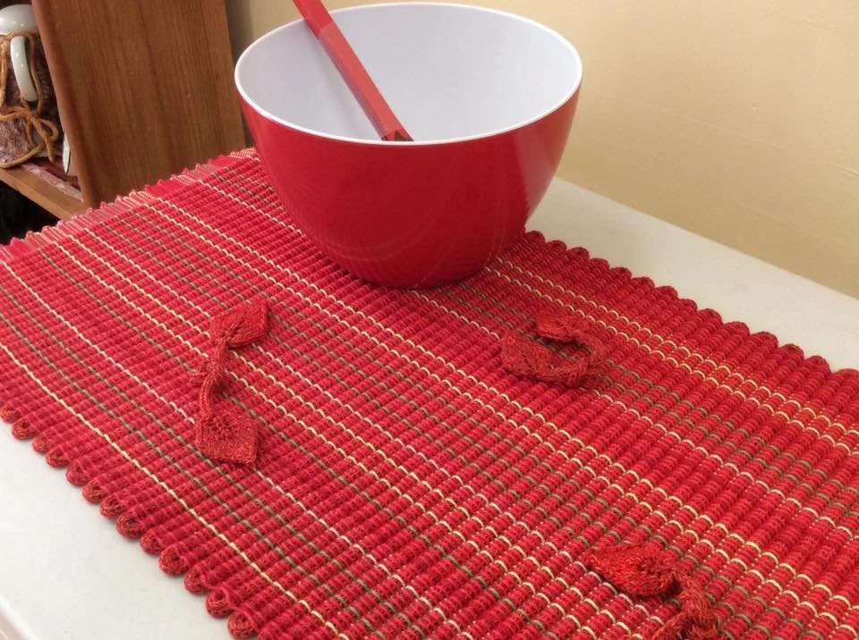 Red table runner with three small red fabric knots, a large red and white mixing bowl with a red spatula inside, on a white table.