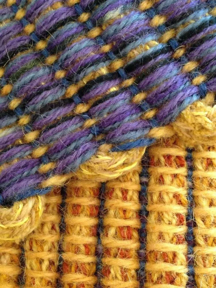Close-up view of multicolored woven or knitted fabric featuring yellow, purple, blue, green, and black yarns.