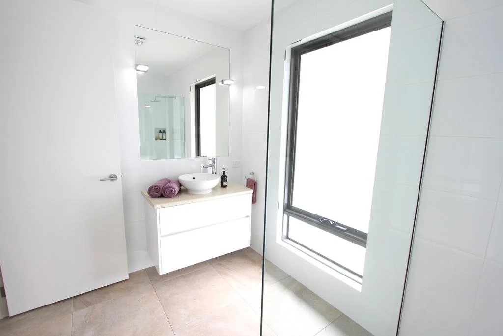 Modern bathroom with white walls, a sink with a countertop, and a large window allowing natural light.