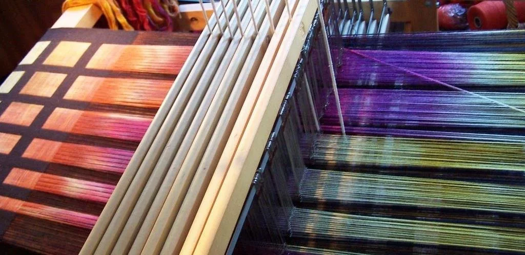 A colorful display of weaving yarns organized by color in a craft store.