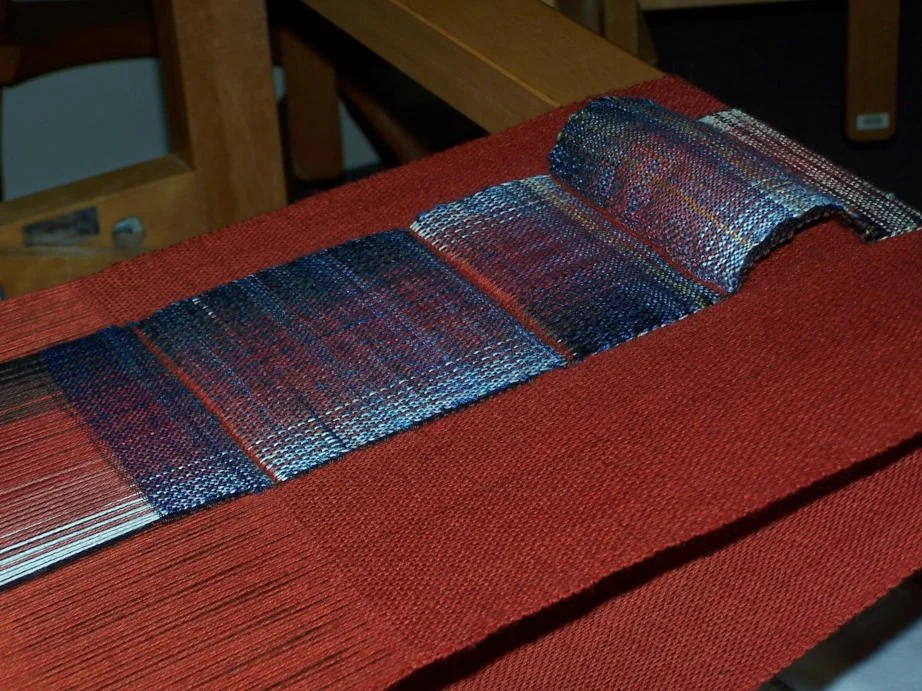 Close-up view of a threaded weaving loom with multicolored threads, set on a red fabric surface, inside a workshop.
