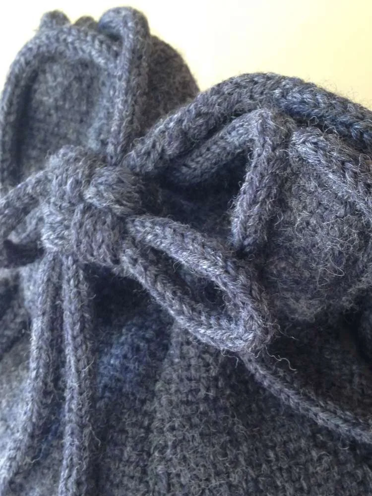 Close-up of a grey knitted scarf or blanket with braided edges.
