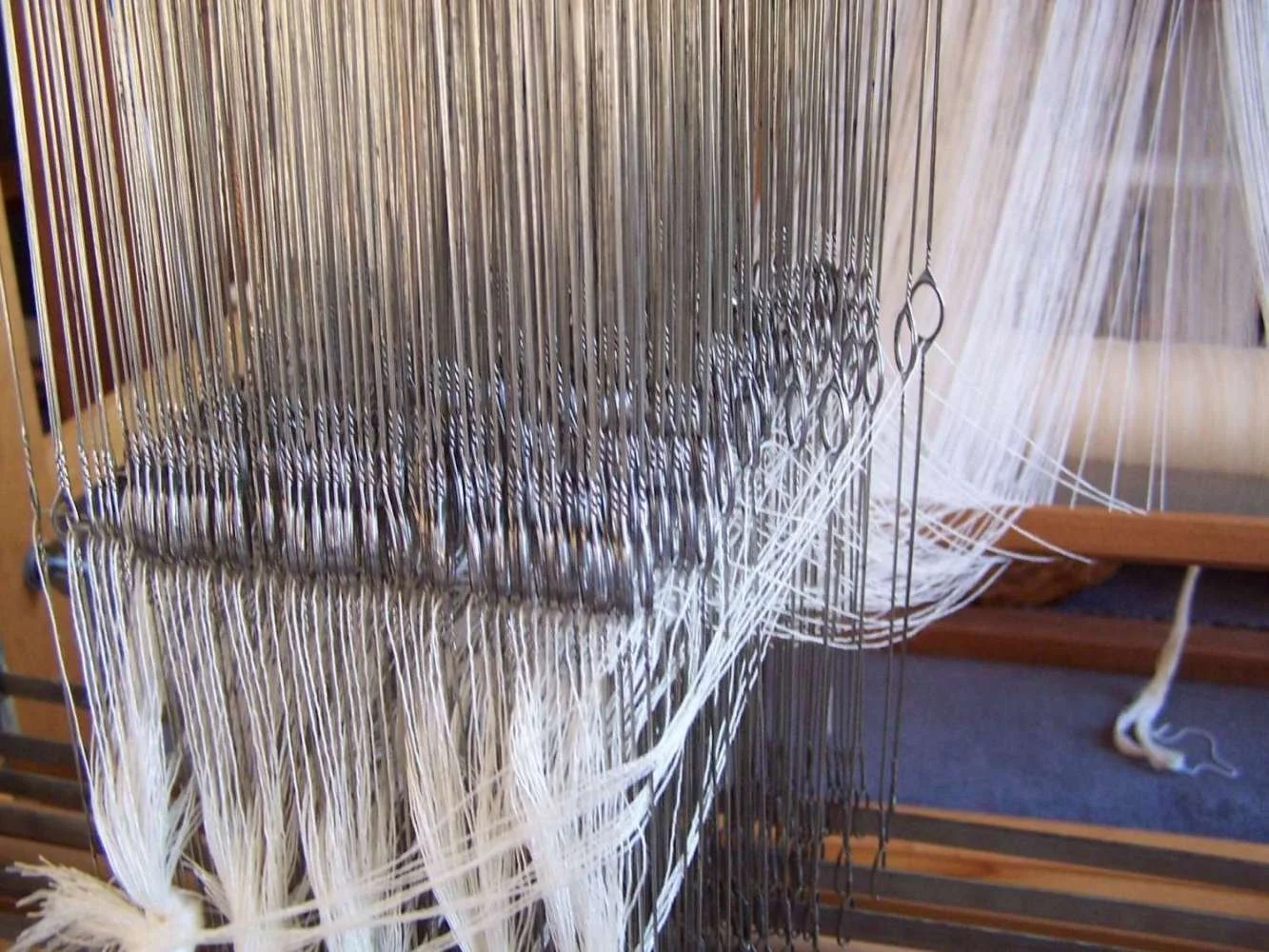 Close-up of a weaving loom with white and dark threads being woven.