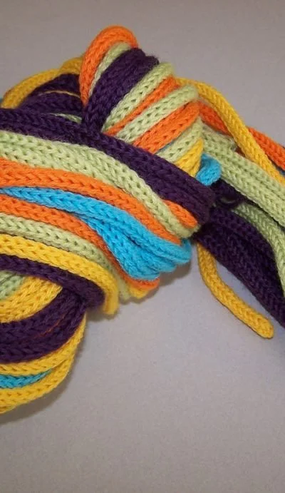 Colorful, striped crocheted yarns tangled on a flat surface.