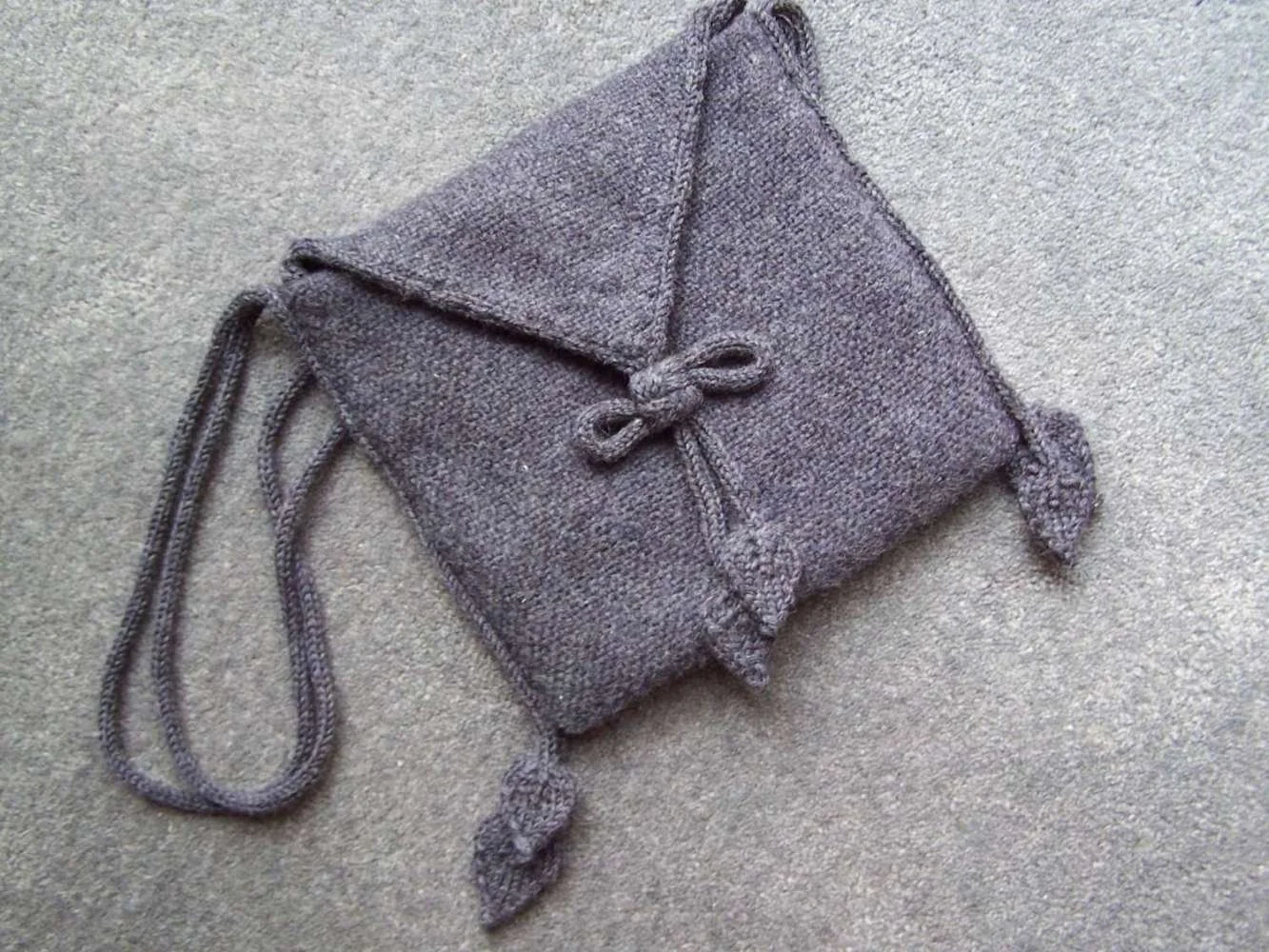 A gray knitted purse with a drawstring closure and decorative tassels, lying on a gray surface.