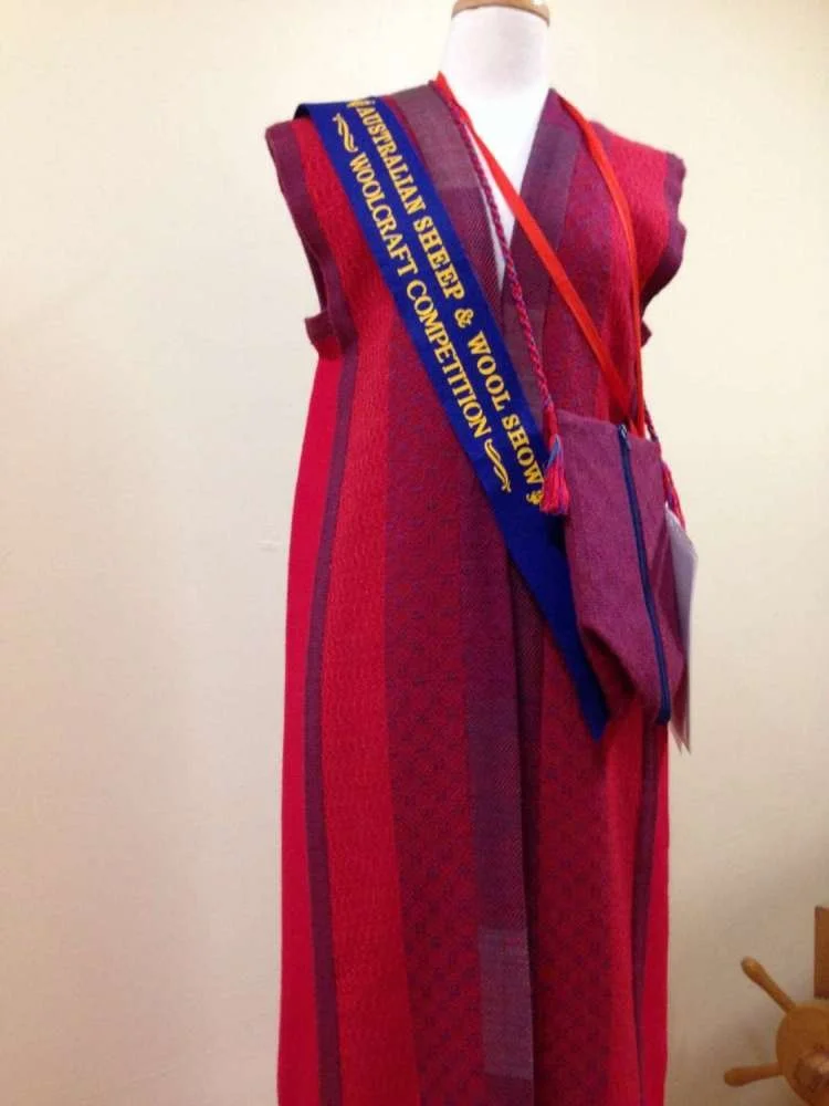 Red and purple woven blanket or shawl draped over a mannequin with a sash from the Australian Sheep & Wool Show and Woolcraft Competition.