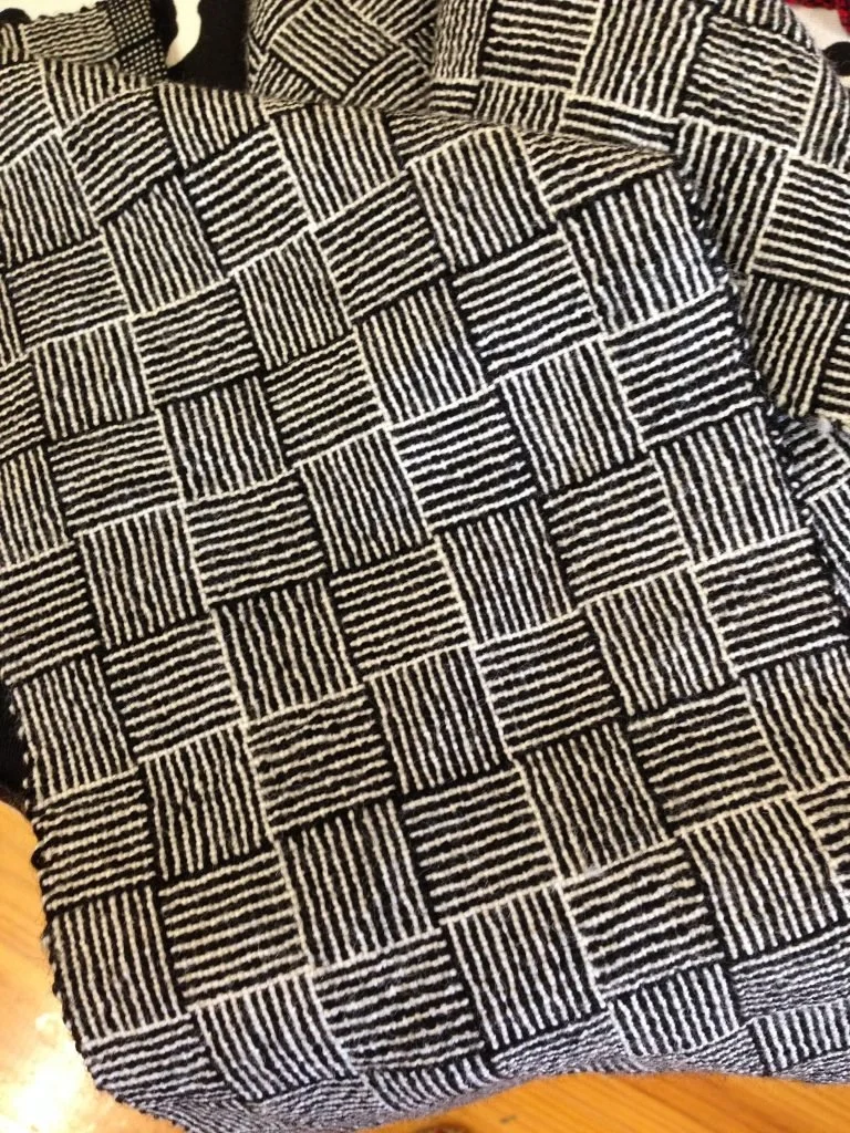 Close-up of a fabric with a black and white checkered pattern, featuring different stripe arrangements in each square.