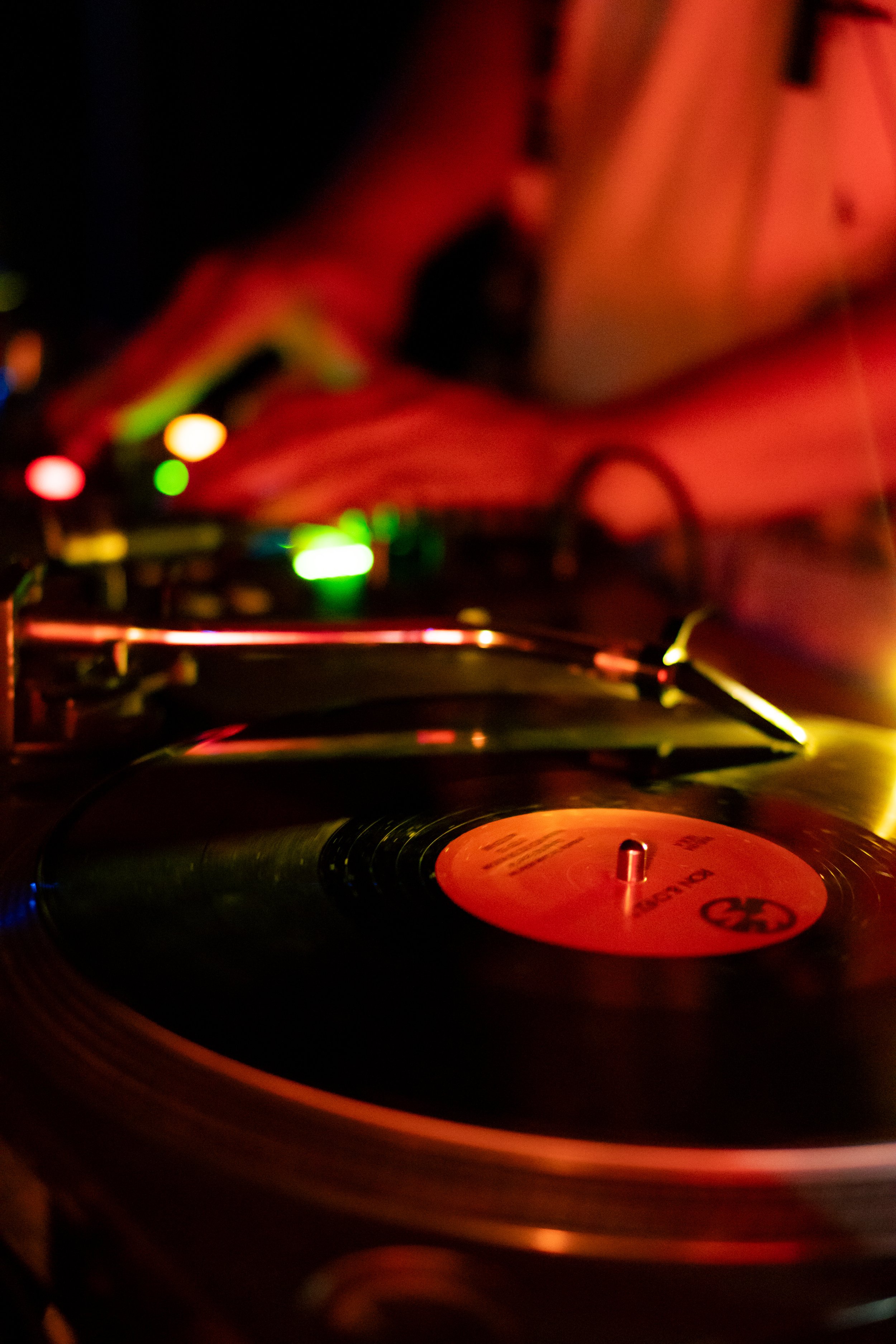 Una tornamesa girando un disco de vinilo en un ambiente con luces de colores, principalmente rojo, amarillo y verde.