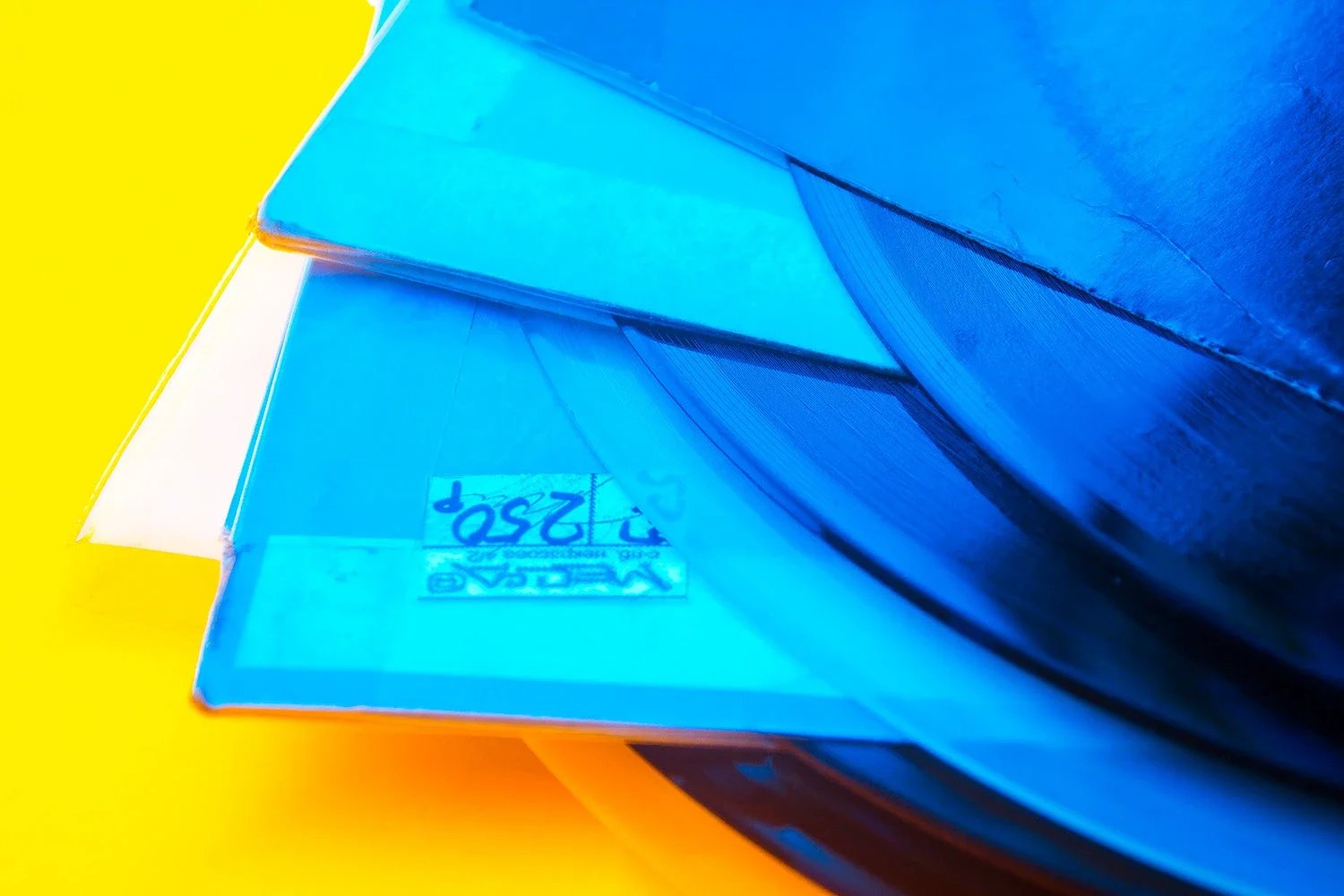 Varios discos de vinilo de musica apilados con una hoja de papel con alguna escritura en azul, todo sobre un fondo amarillo.