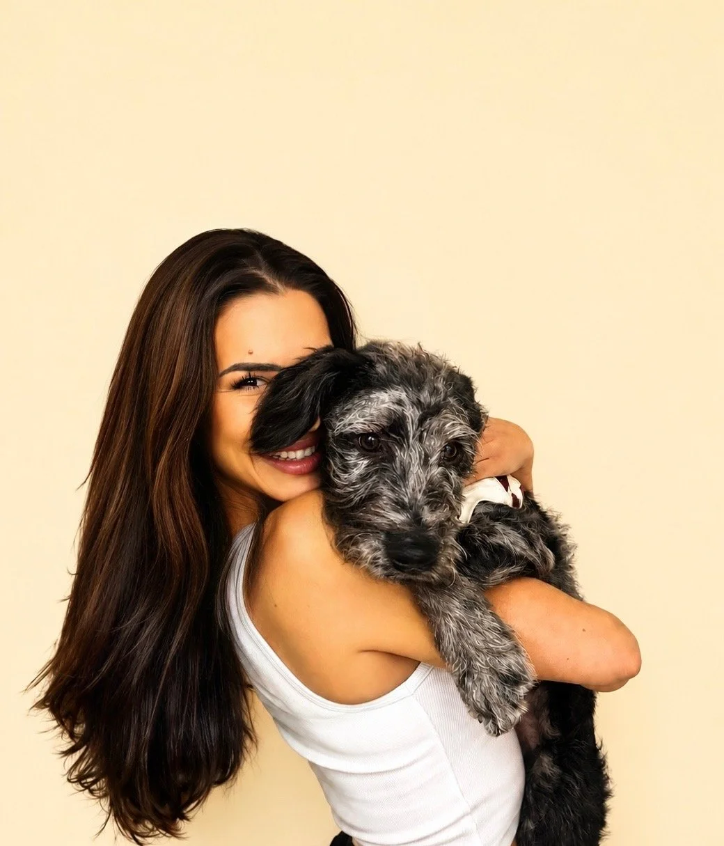 A woman with long dark hair smiling while hugging a black and gray puppy.