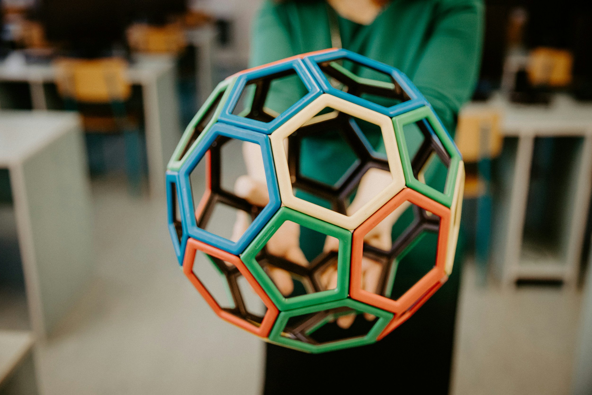 A person in a green shirt holding a geometric sphere made of colorful magnetic building pieces