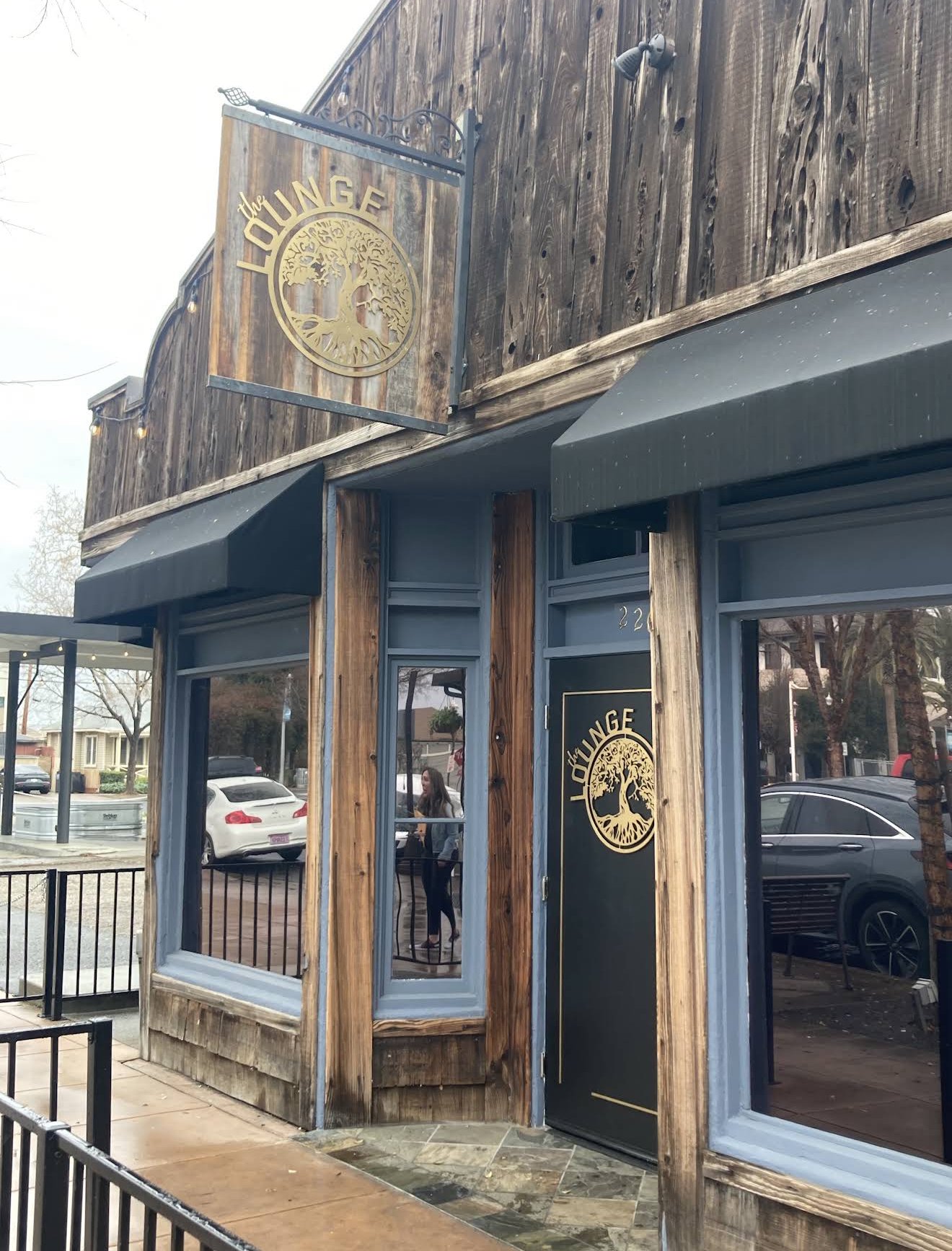 Exterior view of a restaurant named 'The Lounge' with wood paneling and large windows, featuring signs with a tree logo.
