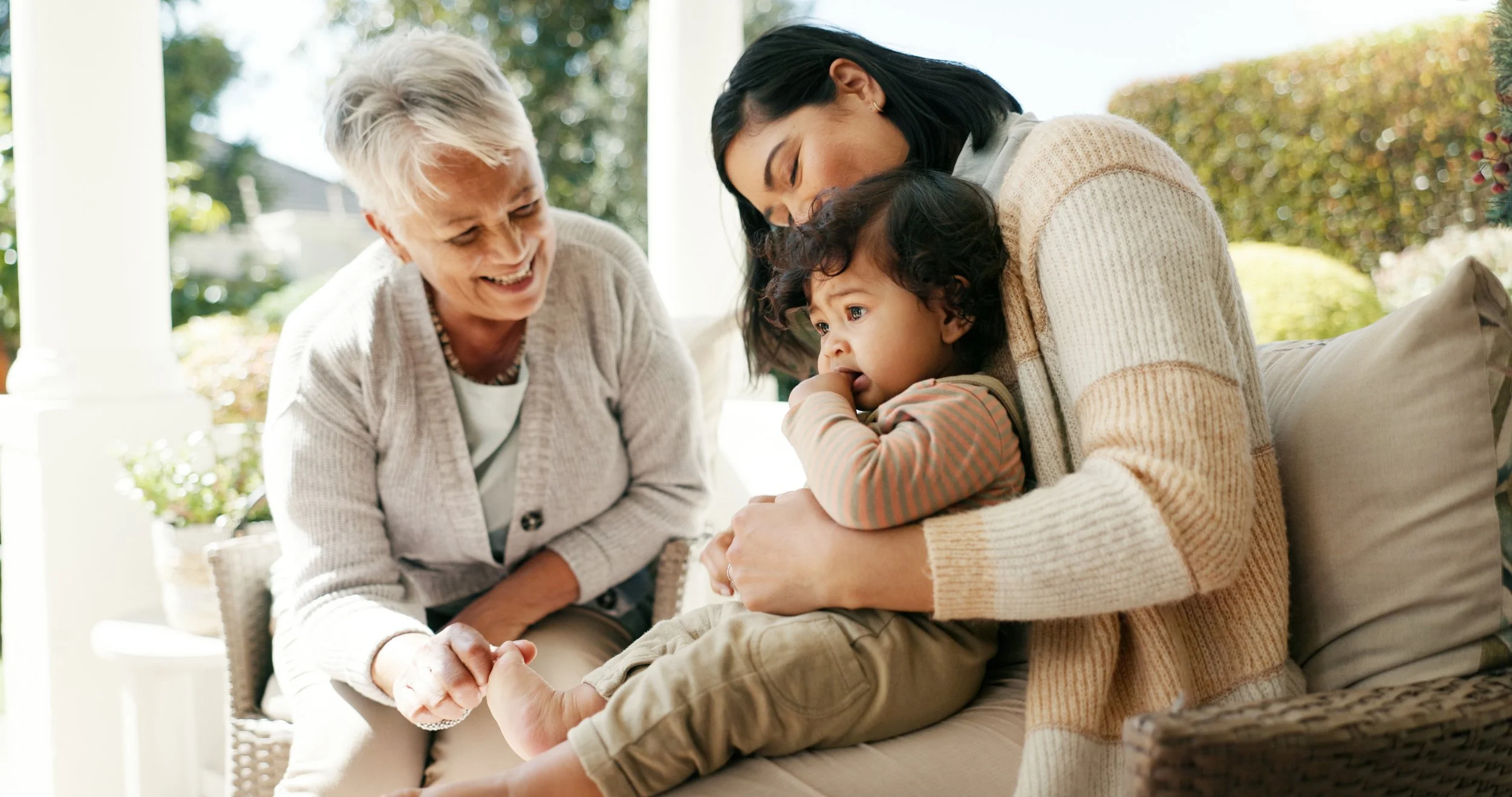 A multi-generational family spending time together outside on a porch, smiling and holding hands, with a blurred natural background.