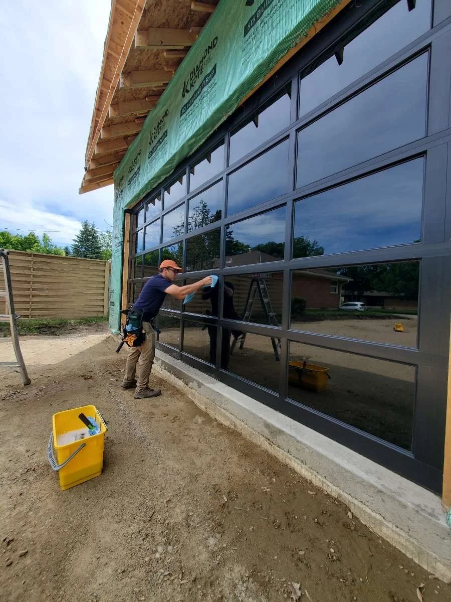 Construction worker cleaning large glass garage doors on a building under construction.