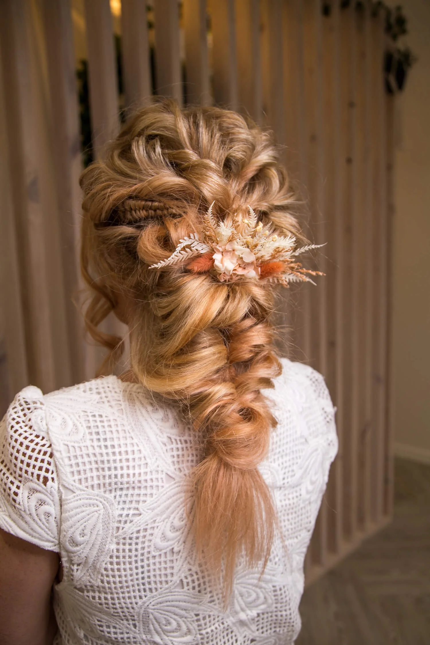 Back view of a woman with long, wavy, orange hair styled in an intricate updo adorned with a floral hair accessory.