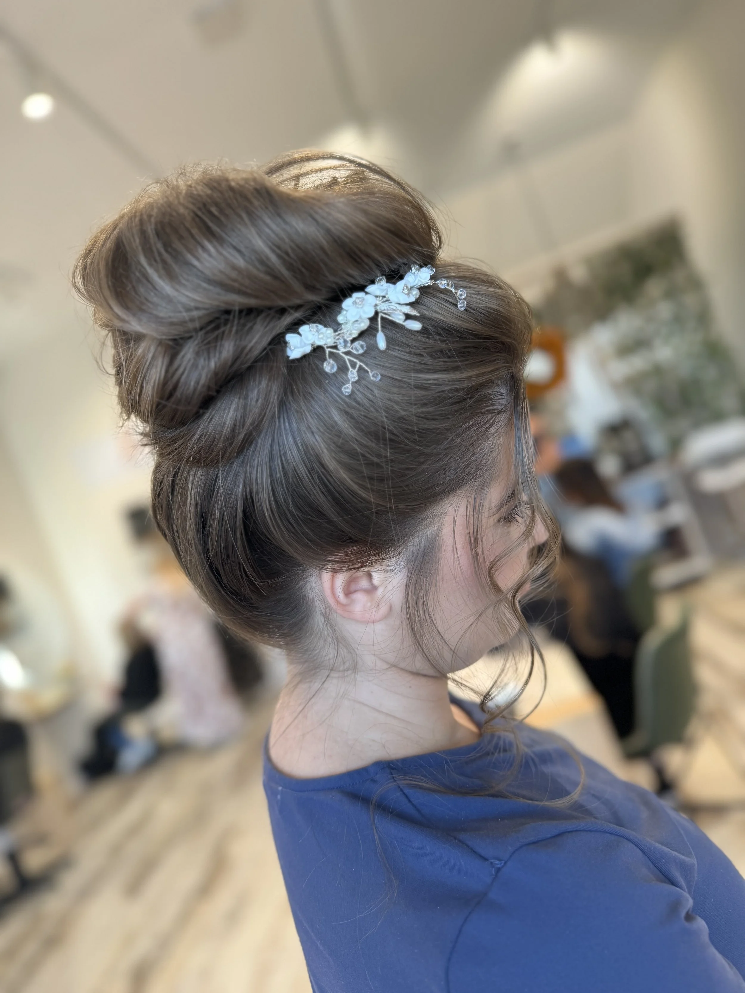 Side view of a woman with styled hair wearing a blue top and a white floral hair accessory, indoors.