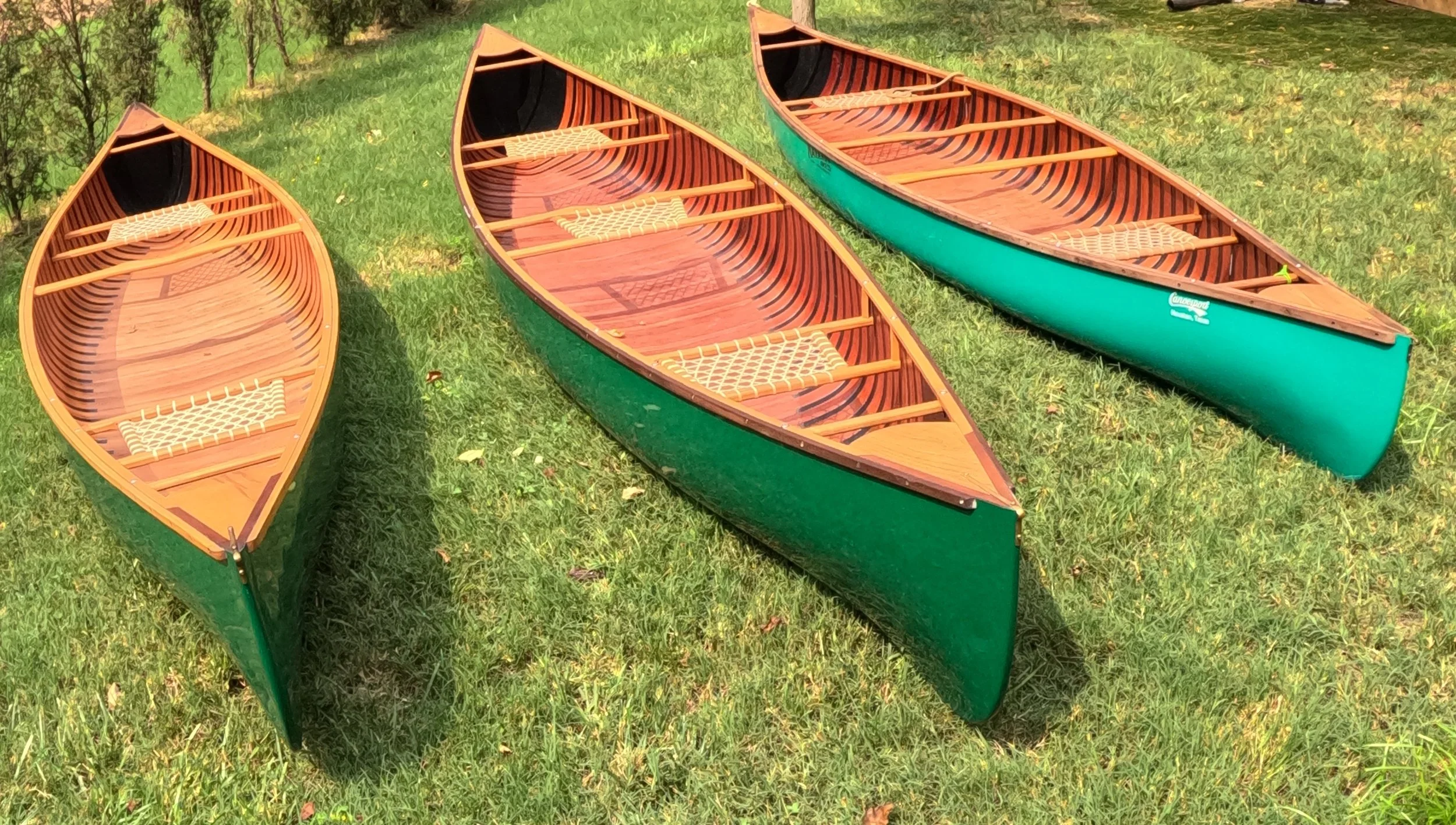 Three colorful wooden canoes placed on green grassy ground with trees and bushes in the background.