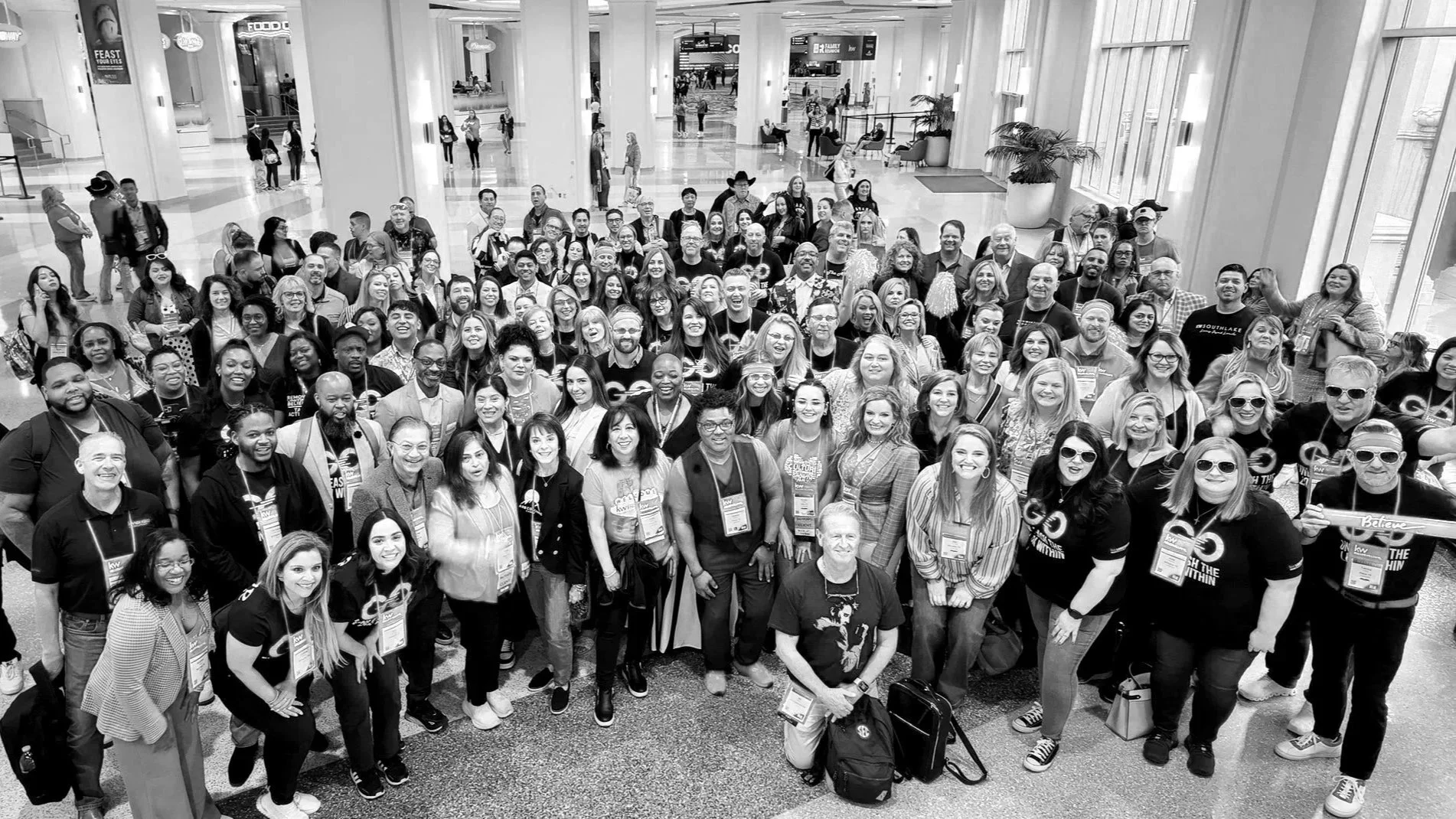 A large group of people gathered in an airport terminal for a group photo, smiling and facing the camera.