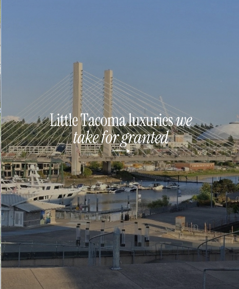 View of Tacoma waterfront with a bridge, boats, and cityscape in the background, overlaid with the text "Little Tacoma luxuries we take for granted."