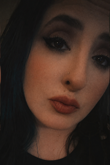 A close-up portrait of a woman with dark hair, makeup including eyeliner, eyeshadow, and nude lipstick.