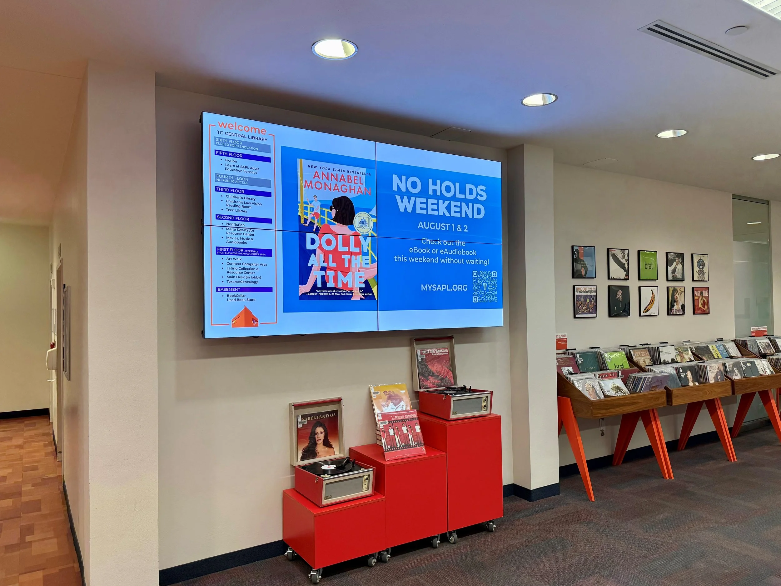 Digital signage content running to promote the No Holds title Dolly All the Time by Annabel Monaghan running in the lobby of the San Antonio Central Library.