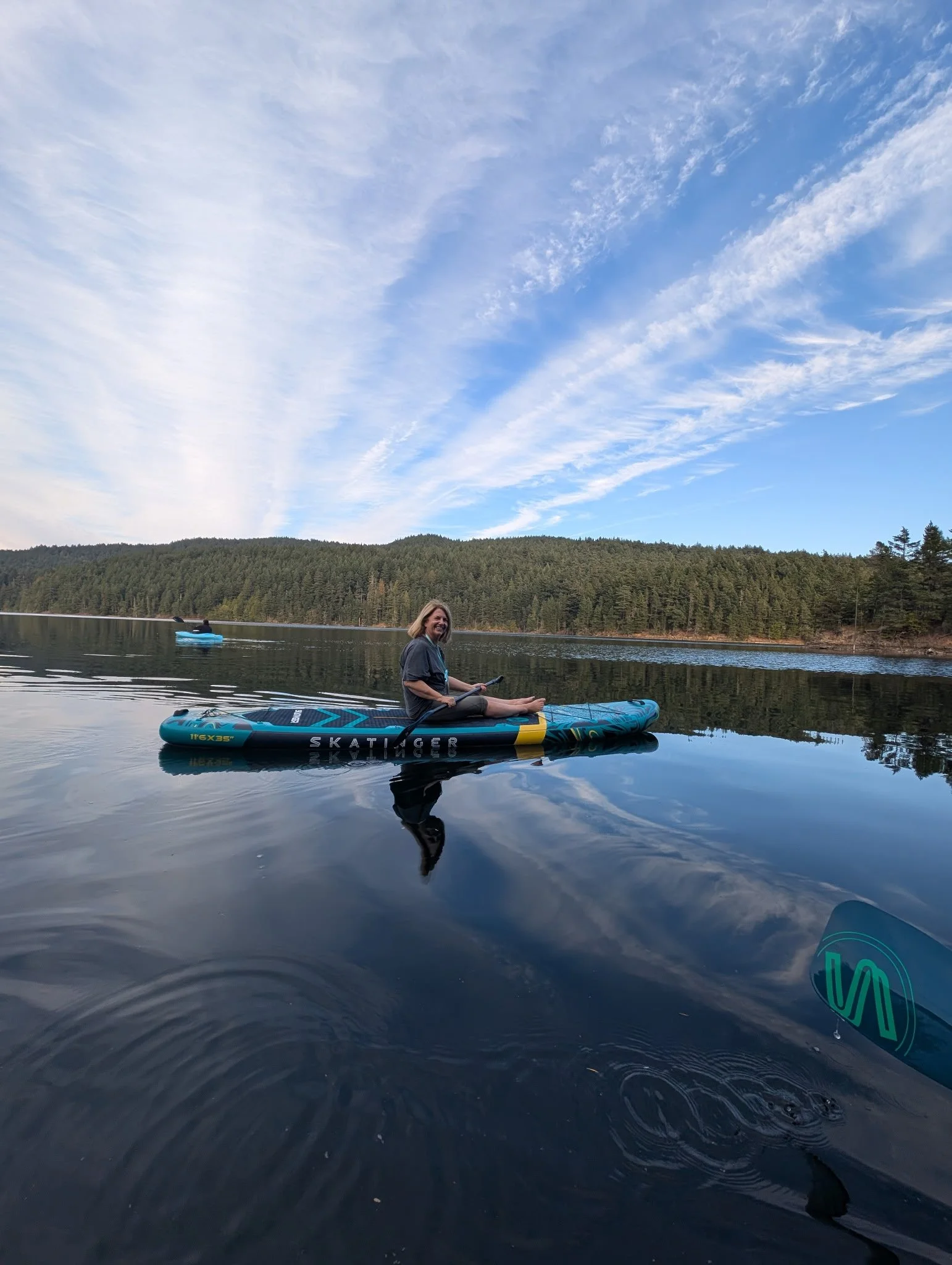 Martina sitting on an inflatable stand-up paddleboard on a calm lake, smiling.