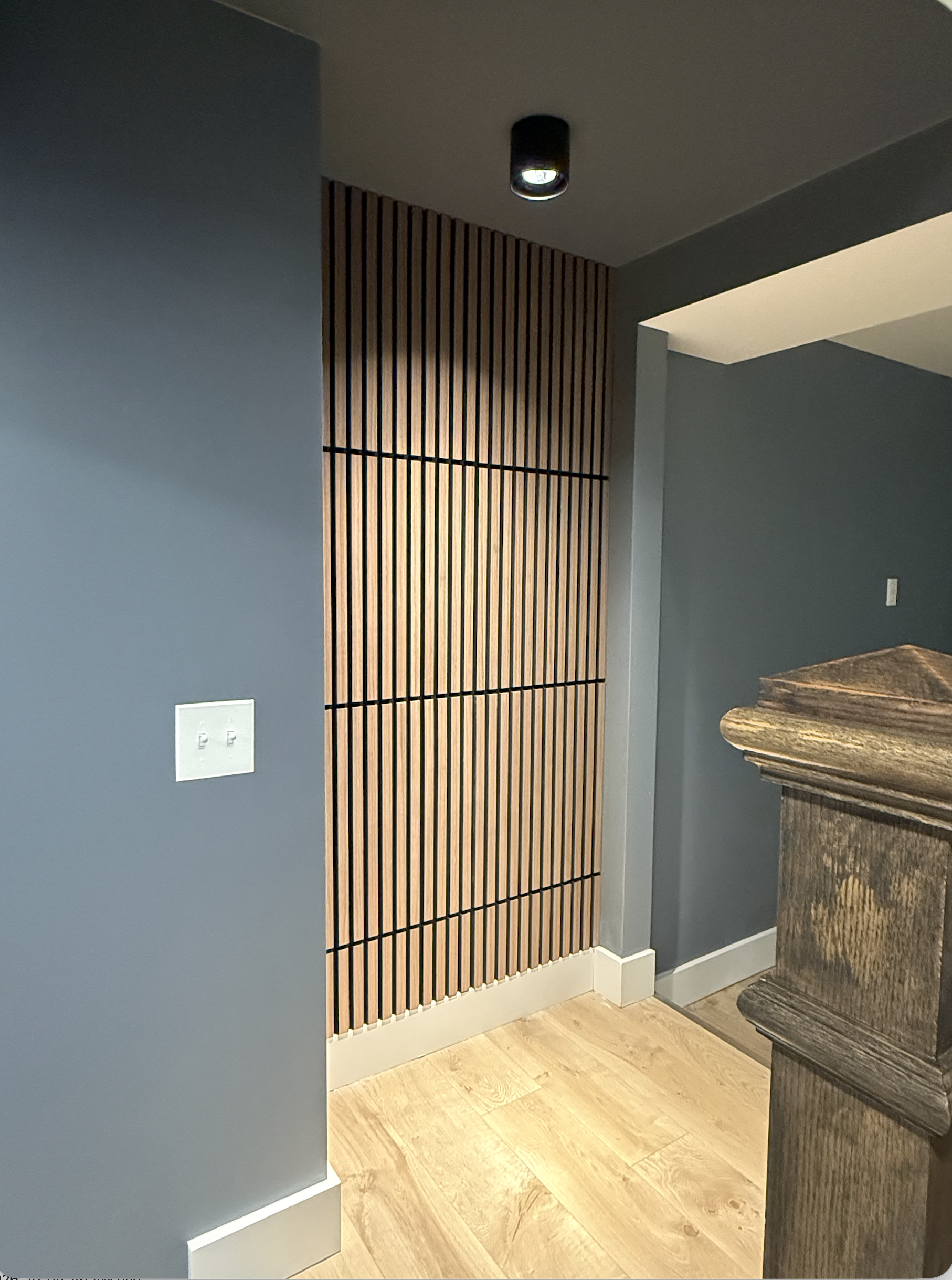 Inside a modern room with blue and gray walls, a wooden slat feature wall, a marble or granite countertop, and hardwood flooring.