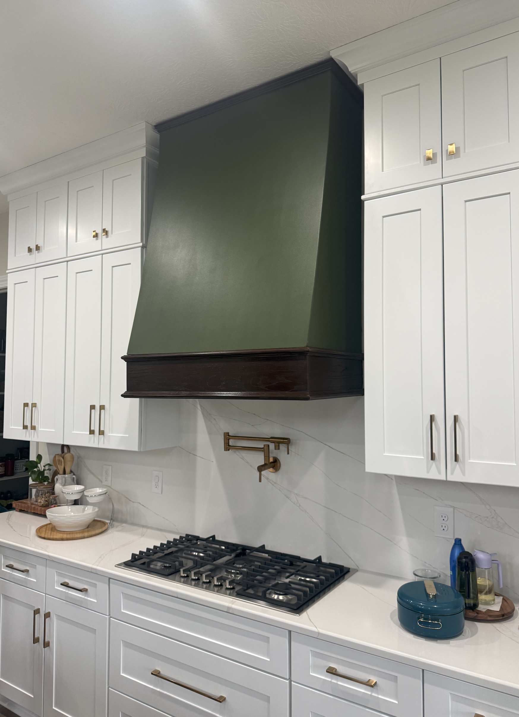 Modern kitchen with white cabinets, marble backsplash, gas cooktop, and a green and dark brown range hood.