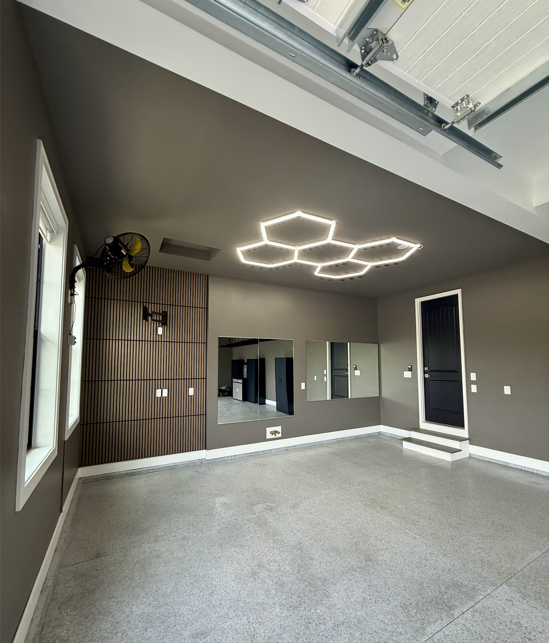 Interior of a modern room with gray walls and floor, featuring a hexagon-shaped ceiling light, a mirror on the wall, black doors, and a small step at the entrance.