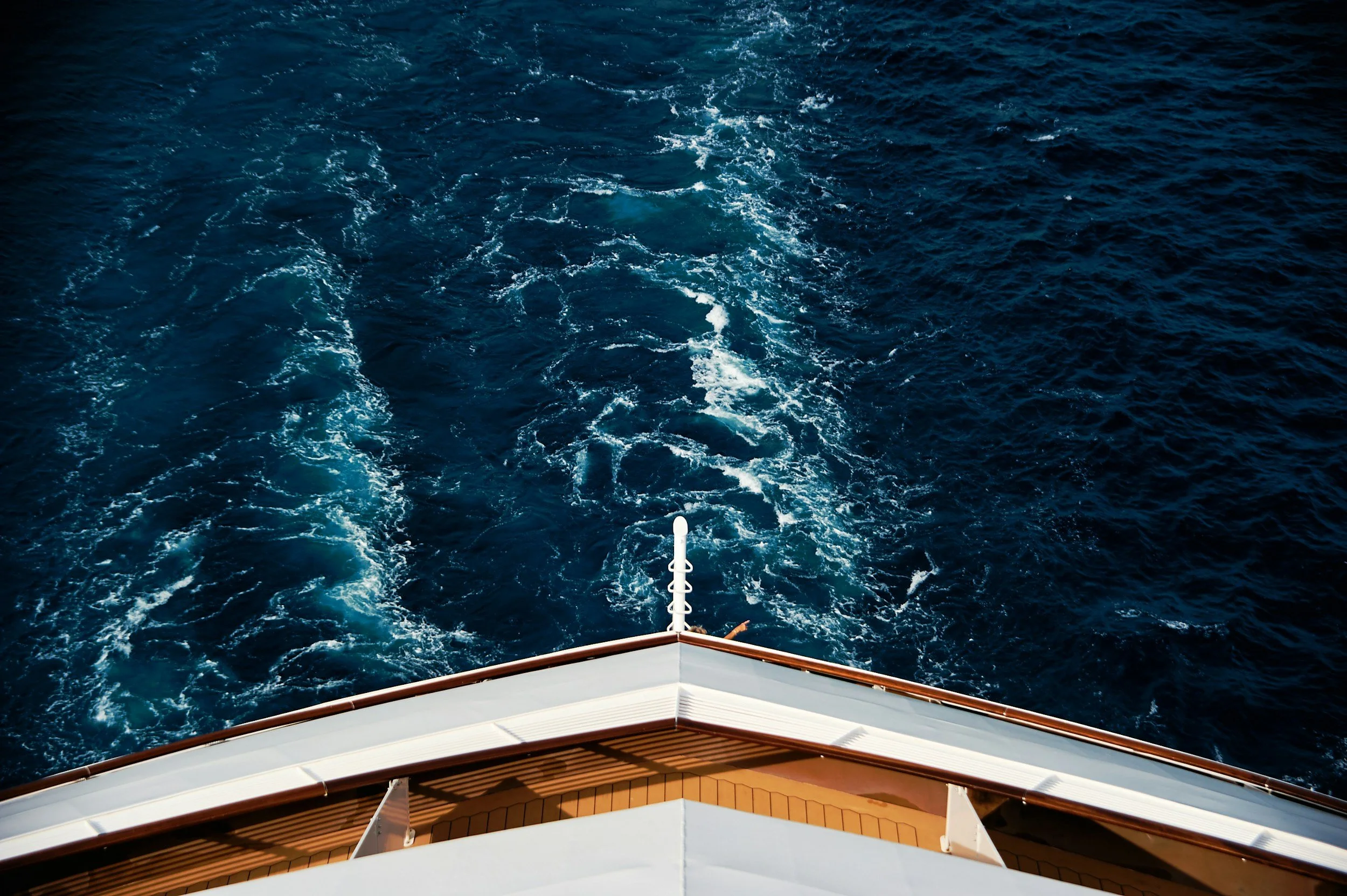 View from the bow of a cruise ship showing the open ocean with a wake trail left by the vessel.