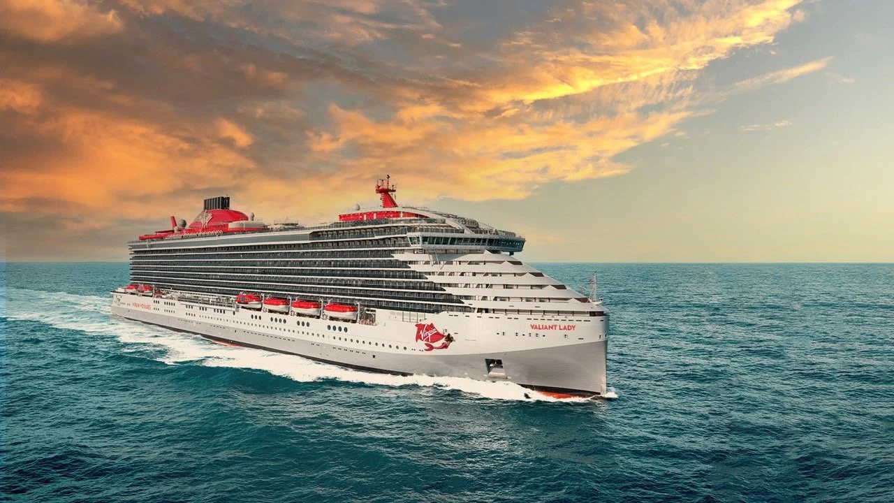 A large white cruise ship with red accents sailing on the ocean during sunset.