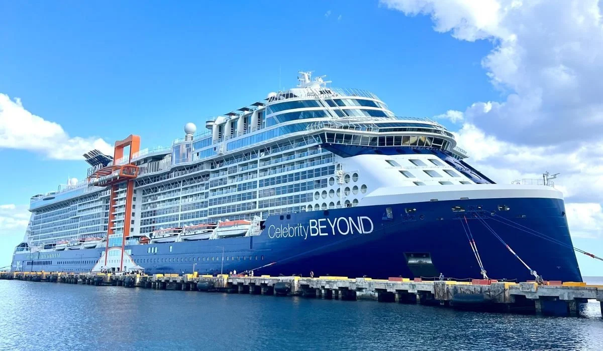 Large cruise ship named Celebrity Beyond docked at a pier with water in the foreground and a blue sky with clouds above.