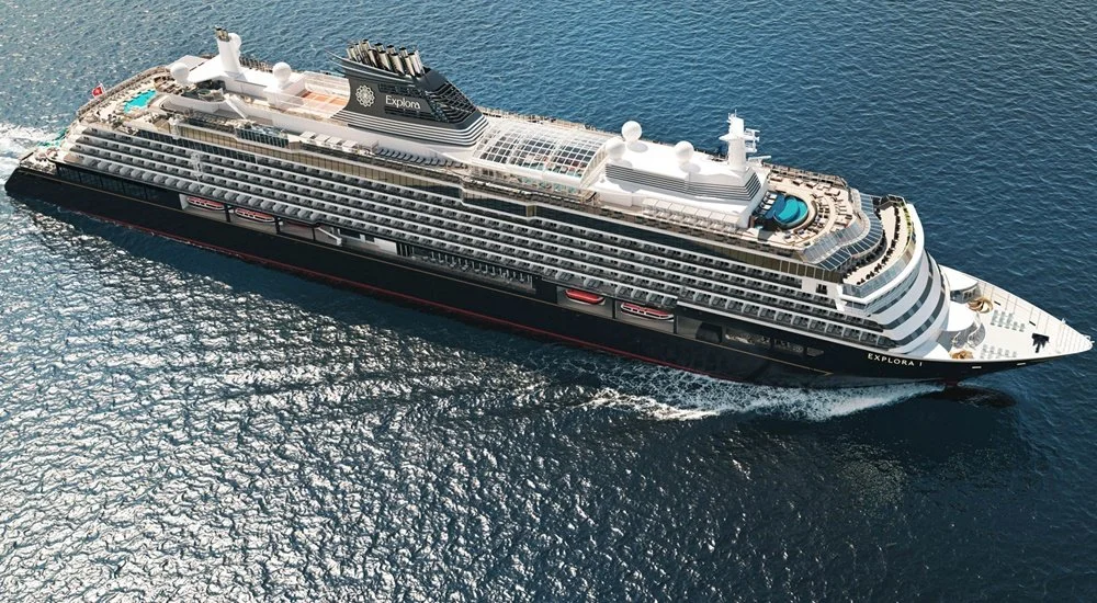 A large cruise ship named Explora sailing on open water with multiple decks, pools, and amenities visible on the top deck.