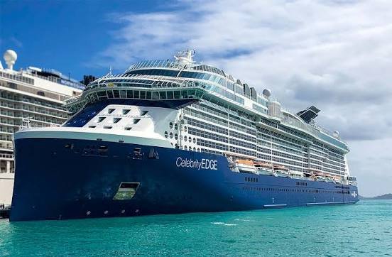 Large cruise ship named Celebrity Edge docked in a harbor with a clear sky.