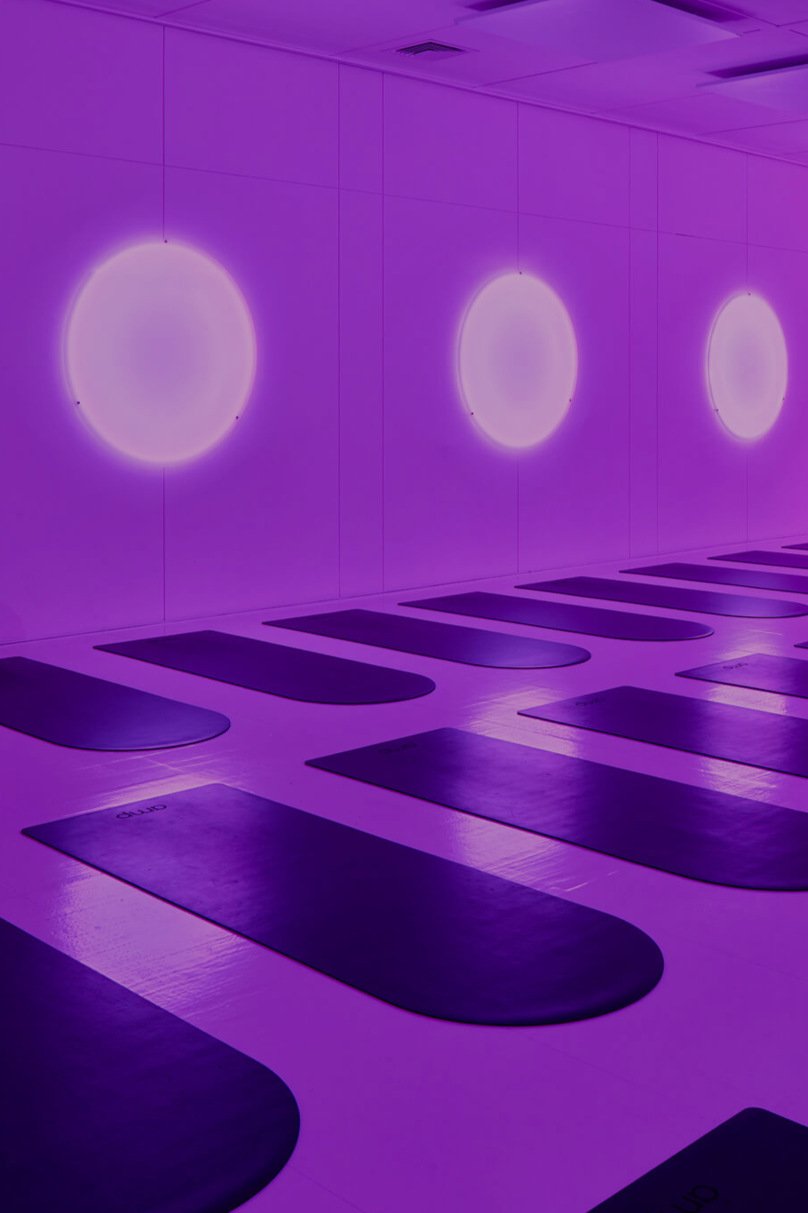 Yoga mats on the floor in a dimly lit room with purple lighting and round glowing wall lights.