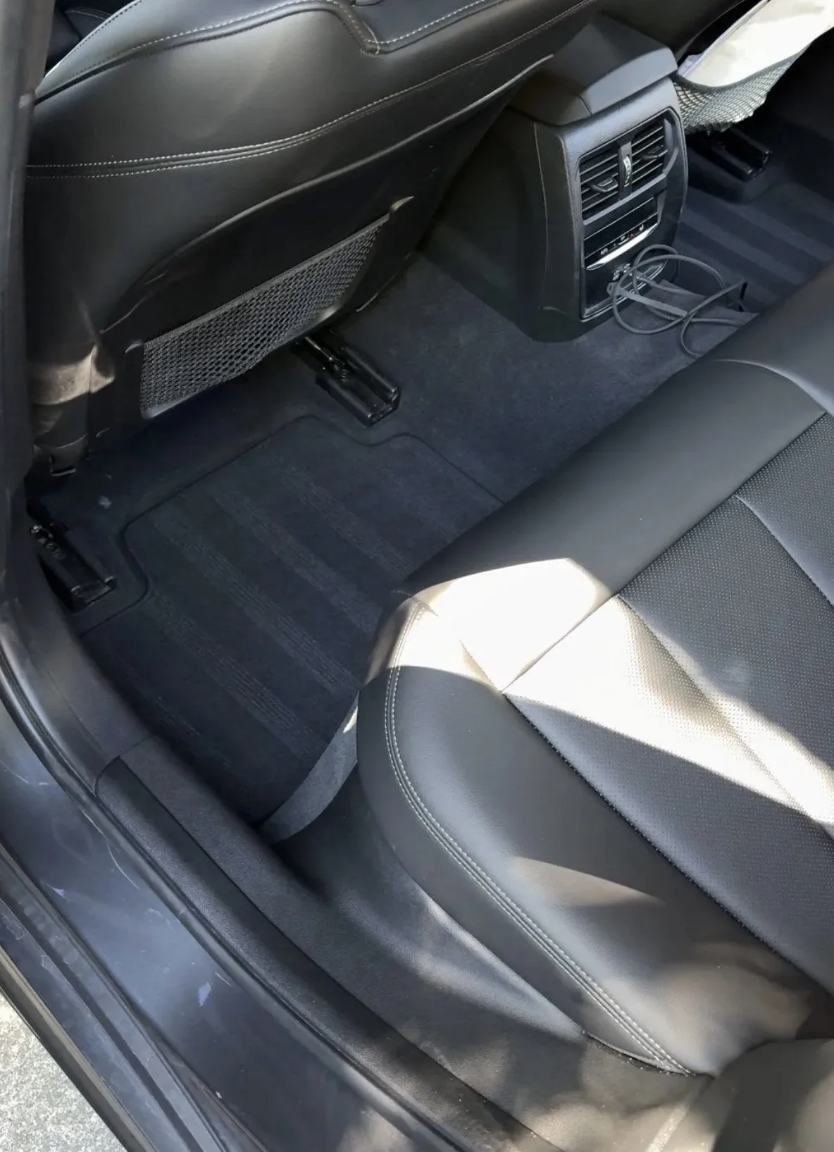 The backseat interior of a car with black leather seats, a black carpeted floor, and rear air vents.