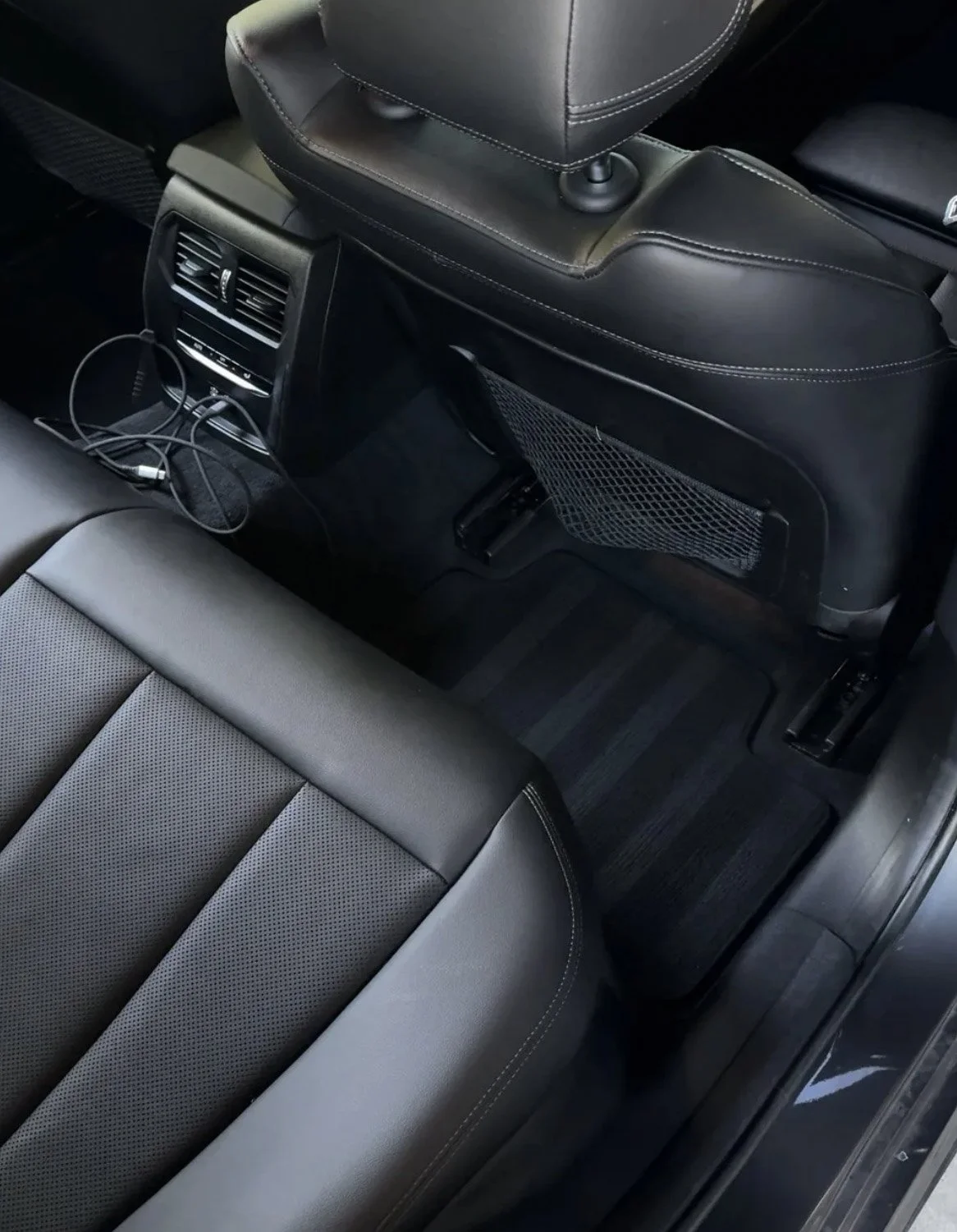 Backseat view of a car interior showing two seats, an air vent with a charging cord, and a storage compartment on the back of the front seat with a mesh pocket.