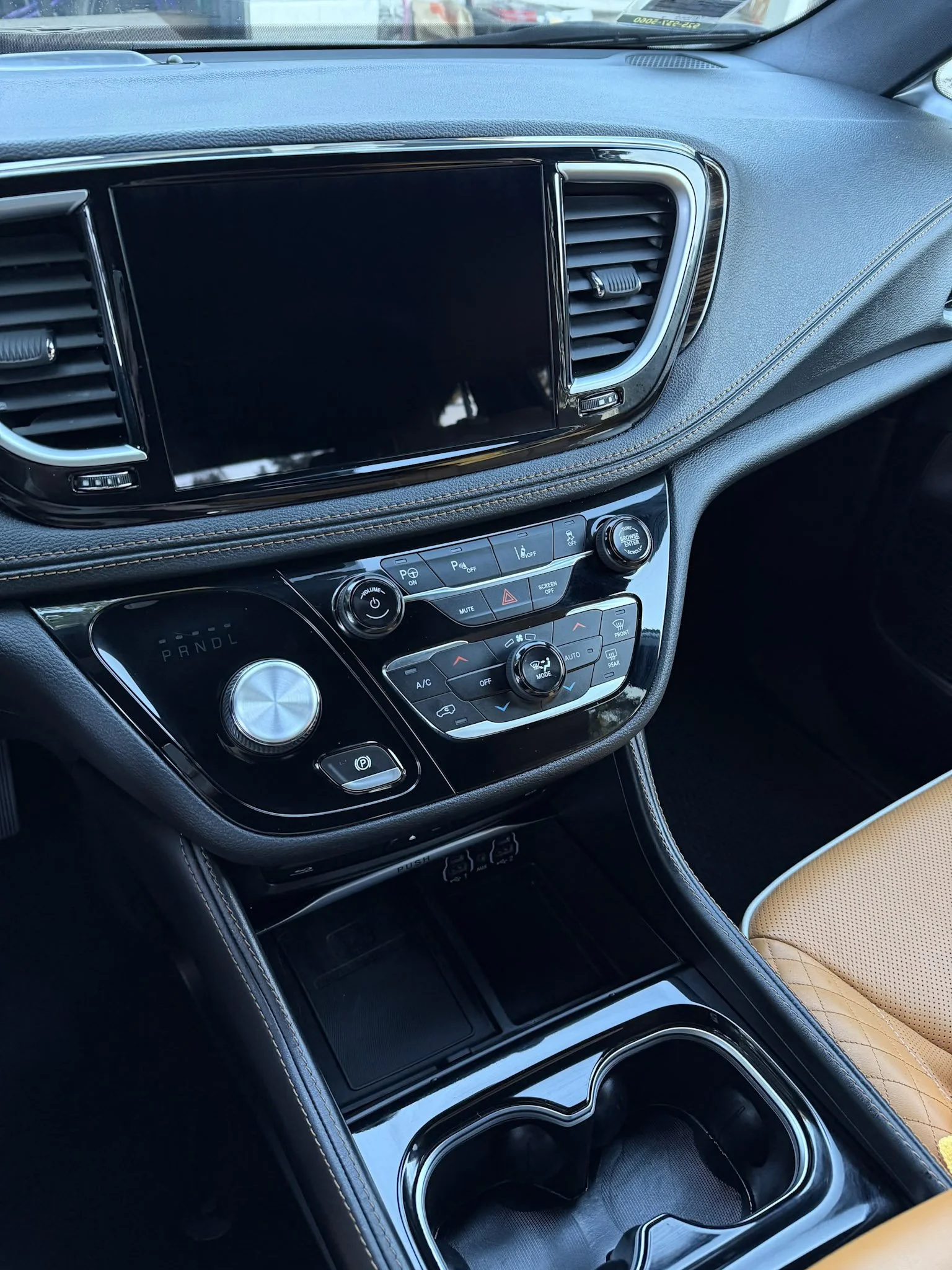 Interior of a car focusing on the center console with a large touchscreen display, climate controls, gear shift, and cup holder.