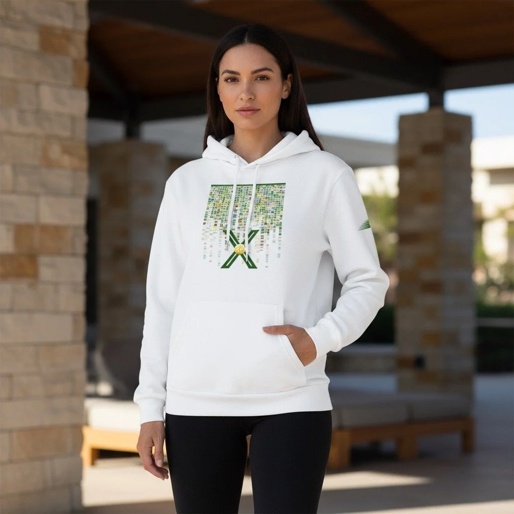 A woman wearing a white hoodie with a pixelated graphic and green accents, standing outdoors near a brick structure with wooden beams.