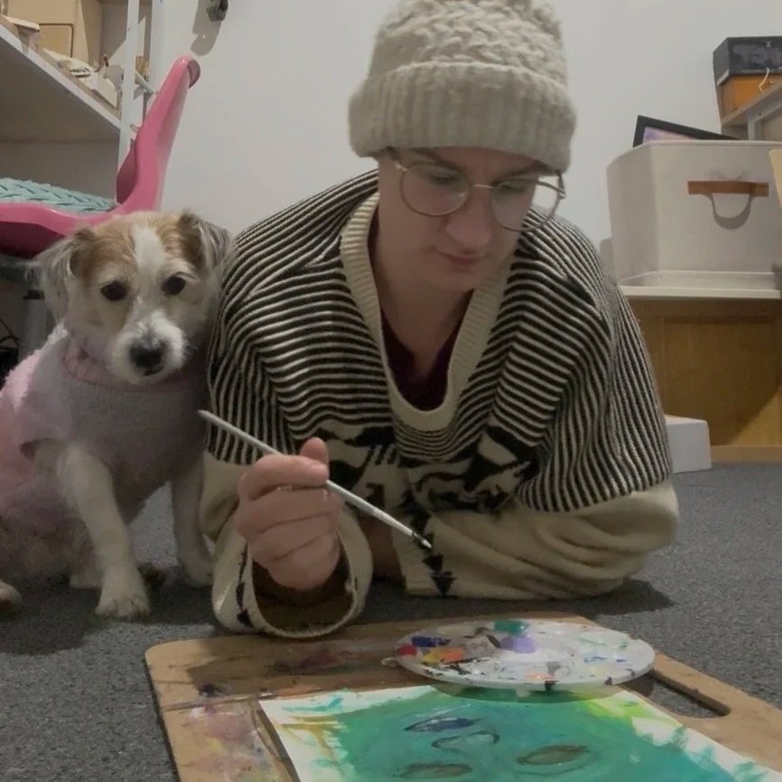 Artist Hannah painting at home with her dog, Sashie, by her side.