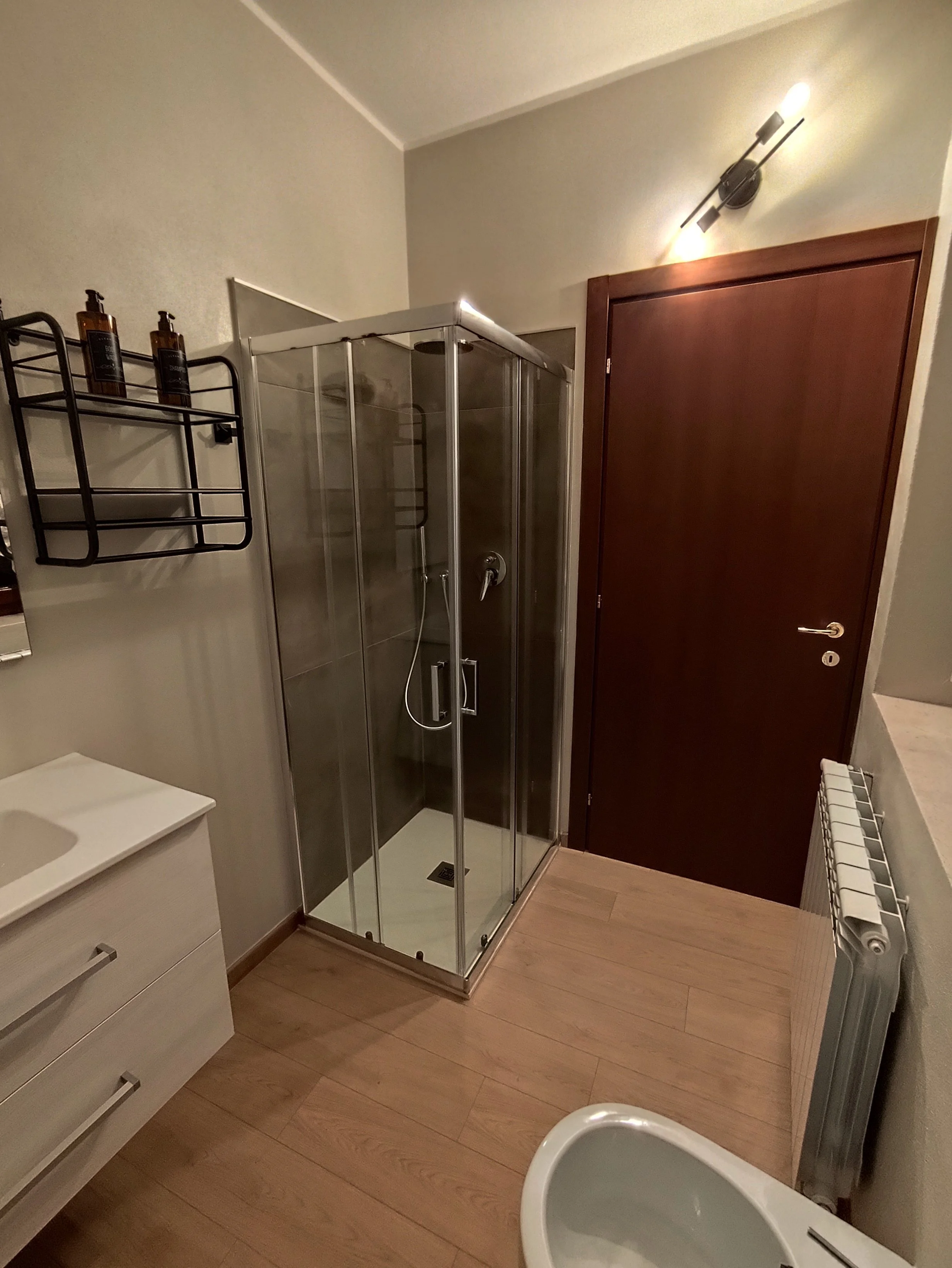 Foto di un bagno con una doccia in vetro, un radiatore, una piccola panca e una parete marrone.