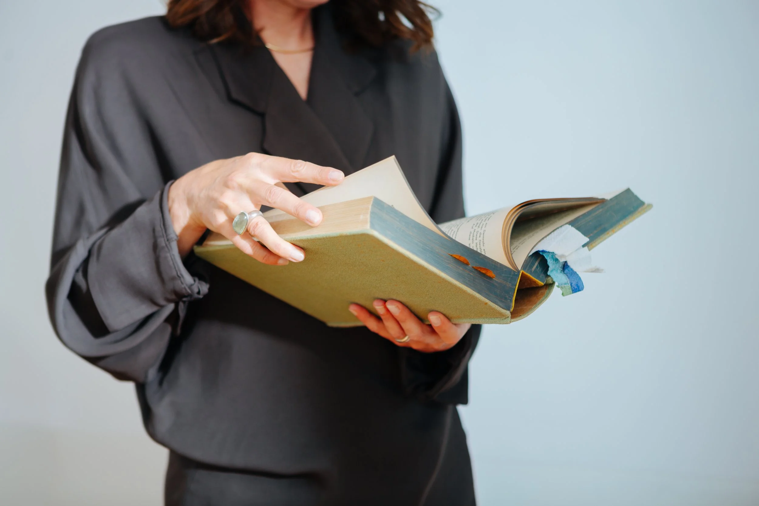 Frau in schwarzem Blazer hält aufgeschlagenes Buch mit bunten Lesezeichen vor einem hellen Hintergrund.