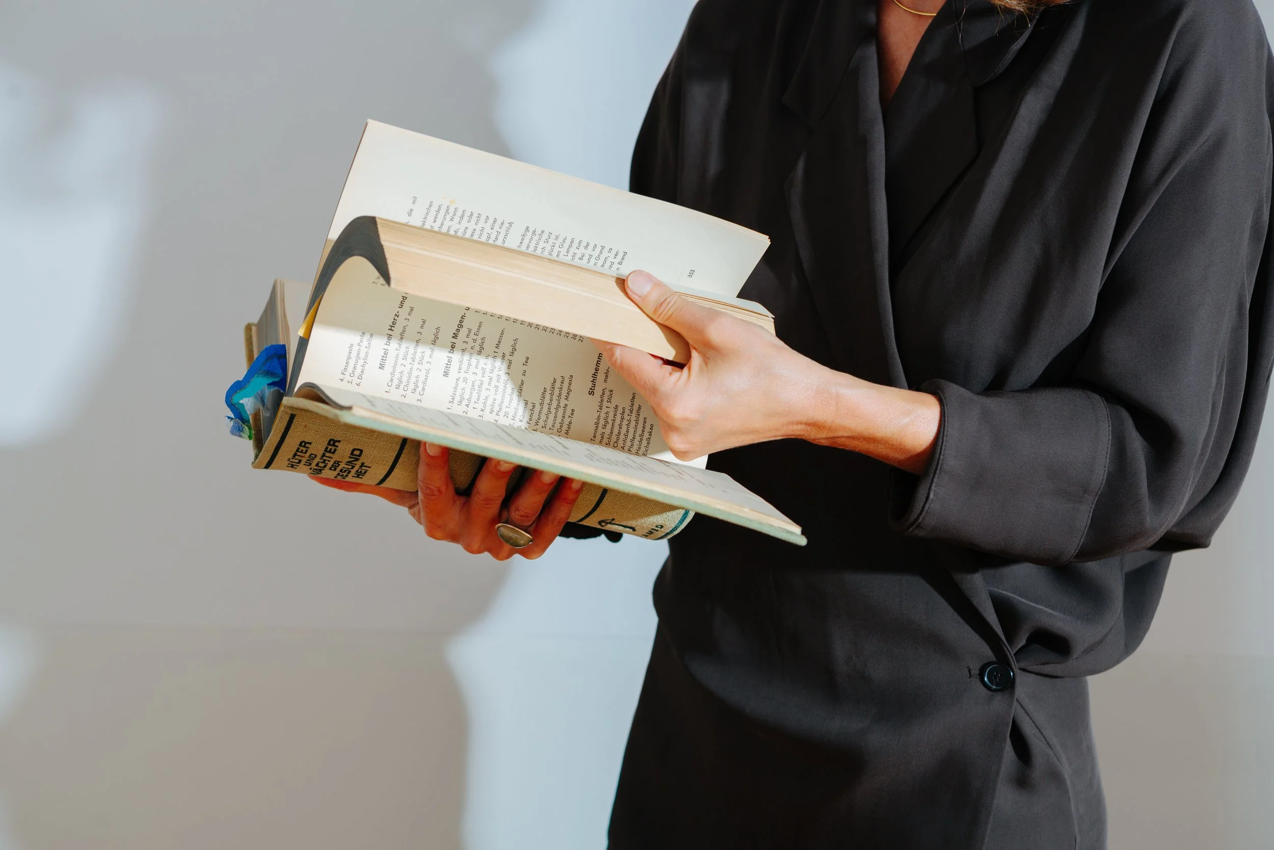 Person in dunklem Hemd liest in einem Buch.