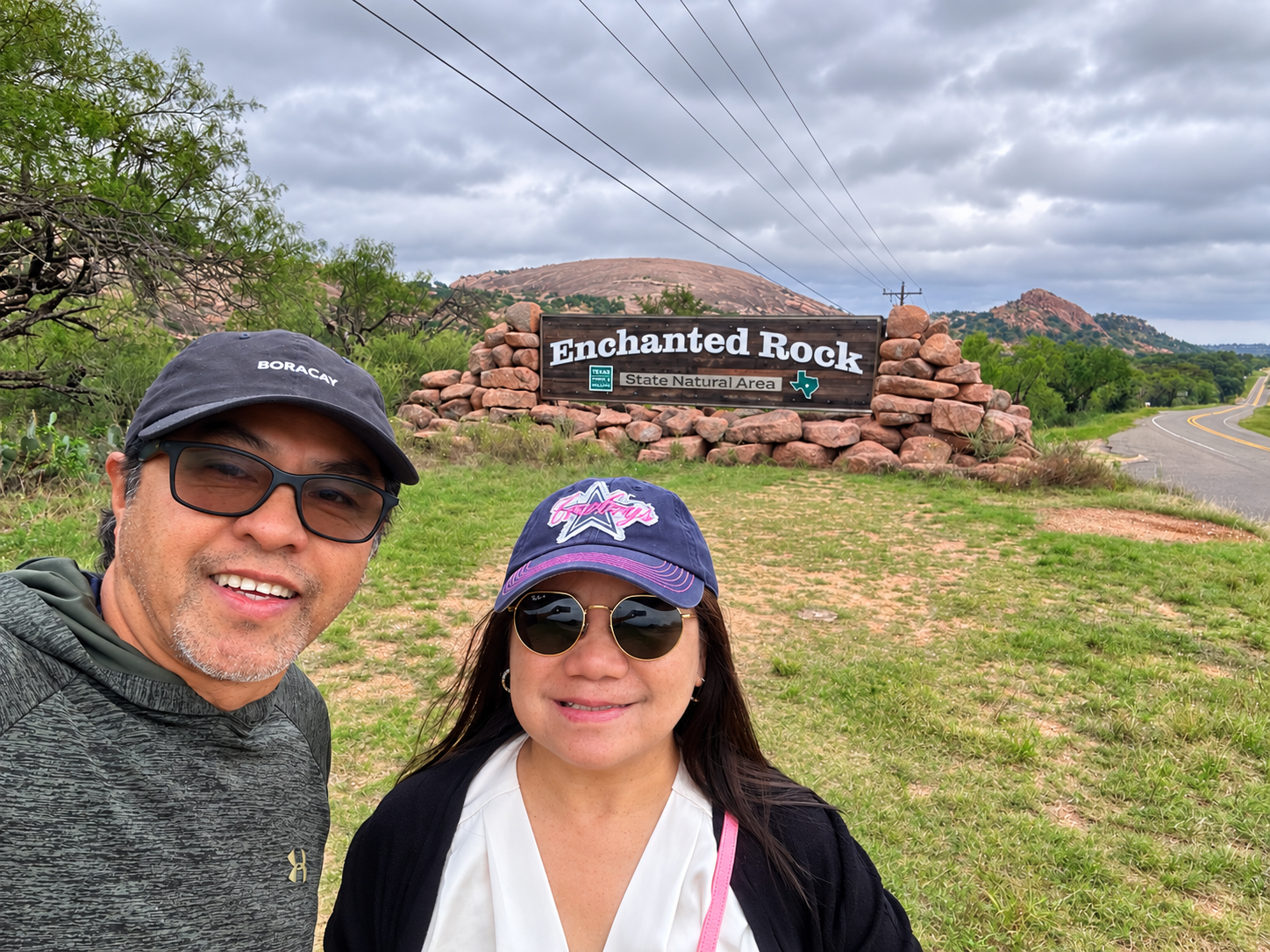 A couple smiling beside the Enchanted Rock State Natural Area entrance sign
